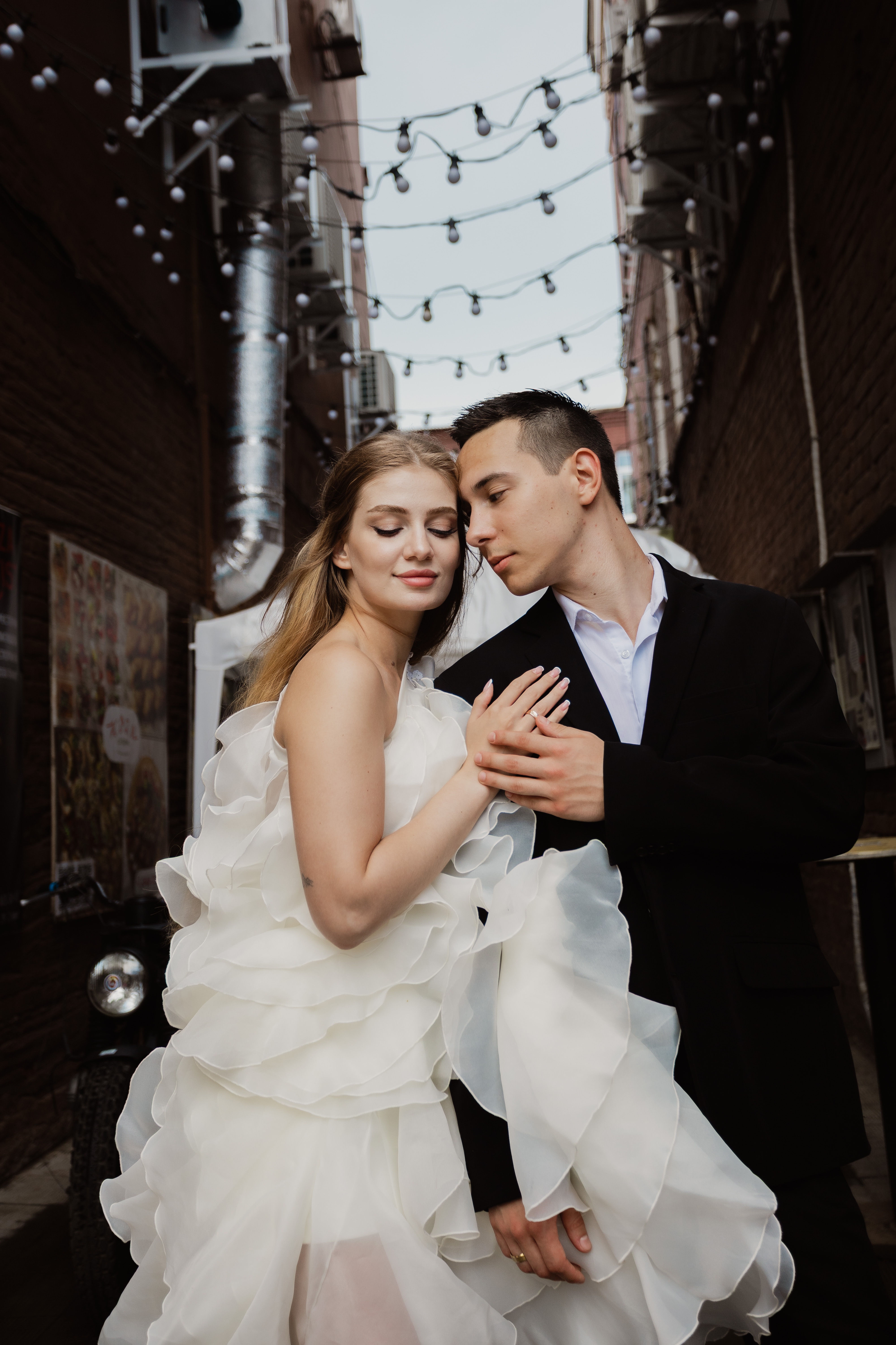Bride and groom kissing tenderly in alley with string lights