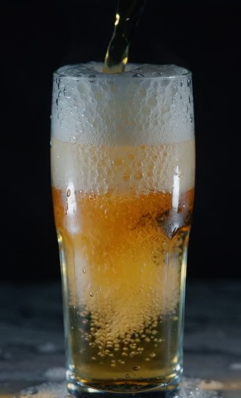 Close-up of cold beer being poured into a frosted glass, bubbles rising rapidly, refreshing condensation on the glass surface, studio lighting, minimalist dark background, 120fps.
